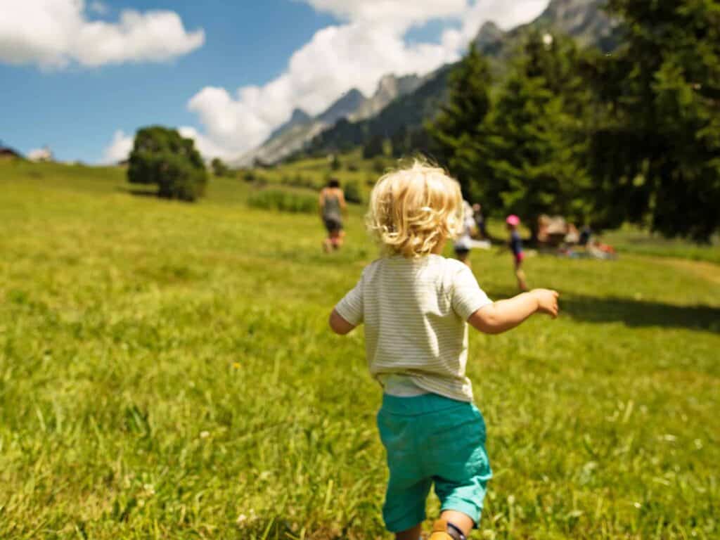 A young toddler running through a sunny alpine field on a family holiday in the French Alps.