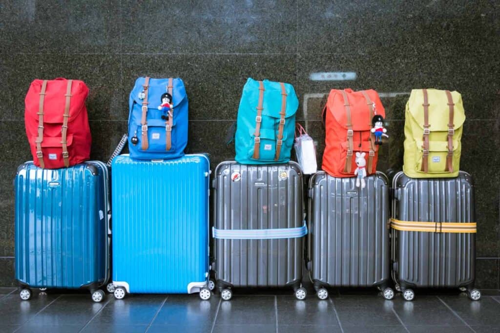 Cinq valises et cinq sacs à dos colorés alignés dans un aéroport, prêts à embarquer pour des vacances d'été en famille.