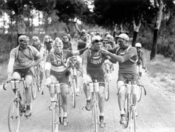 Three Tour de France cyclists sharing a cigarette while riding