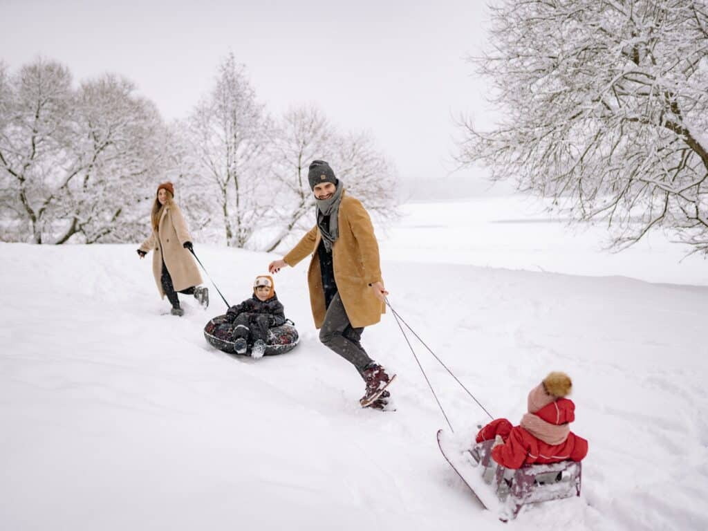 A family enjoying the snow by going sledging.