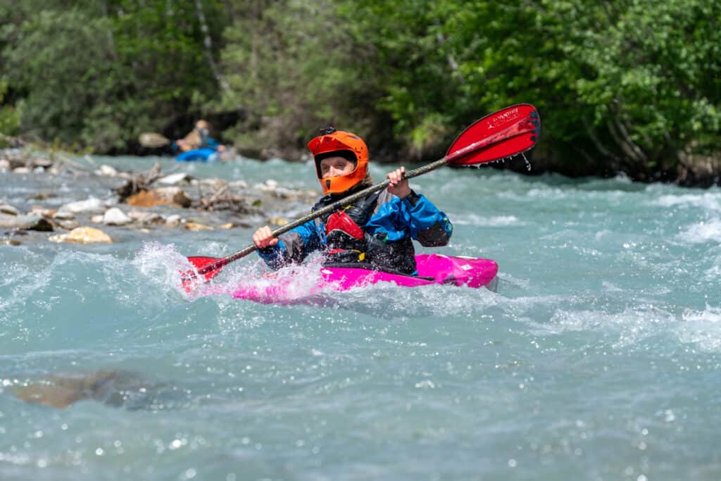 A woman kayaking down a rough river, wearing a helmet 
