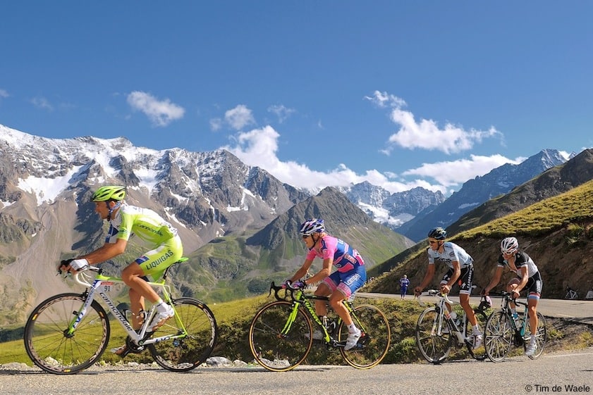 Cyclists tackle a steep climb in front of snowy peaks