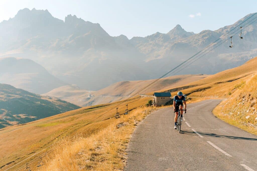 A chairlift passes overhead as a cyclist takes on a mountain road on a hot day