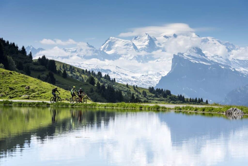 Three cyclists on a path around a lake, with snowy peaks behind them