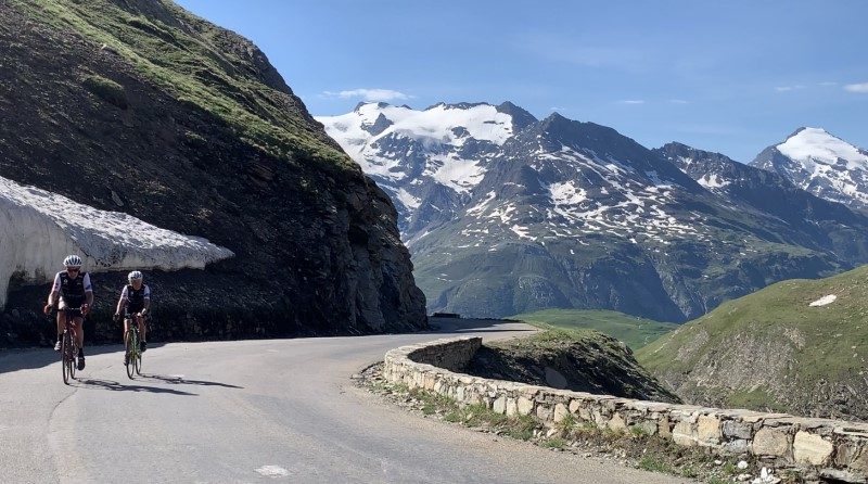 Cyclists climbing a road surrounded by snow-capped mountains