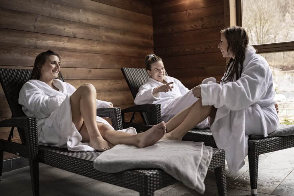 Three women wearing robes relax on deck chairs at the spa