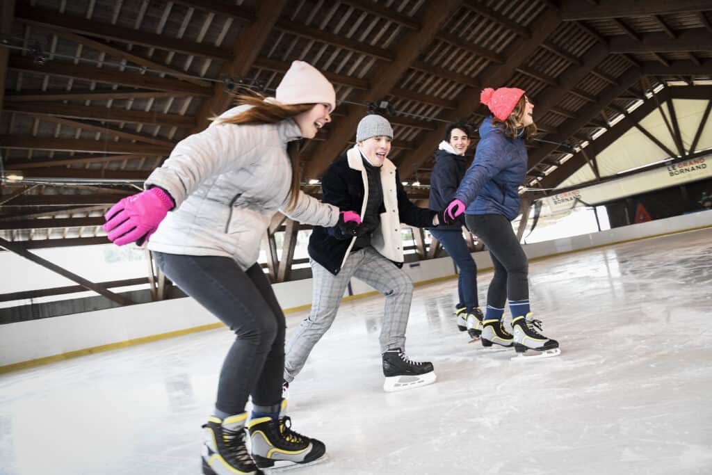Four friends link arms and ice skate in an indoor rink