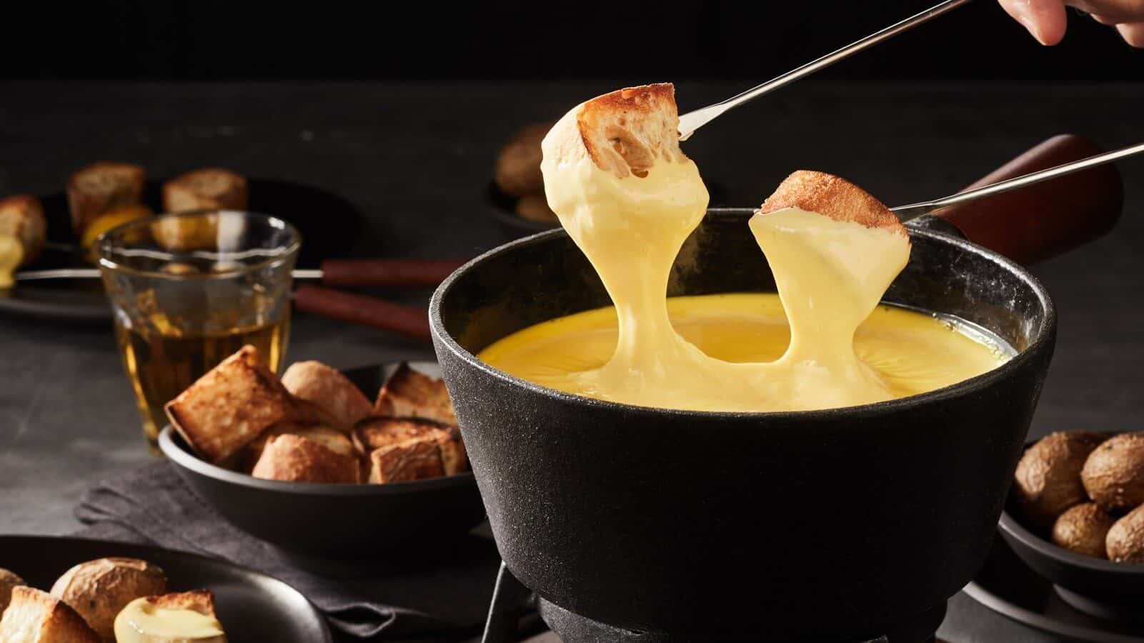 Two pieces of bread are dipped into a fondue pot  of melted cheese