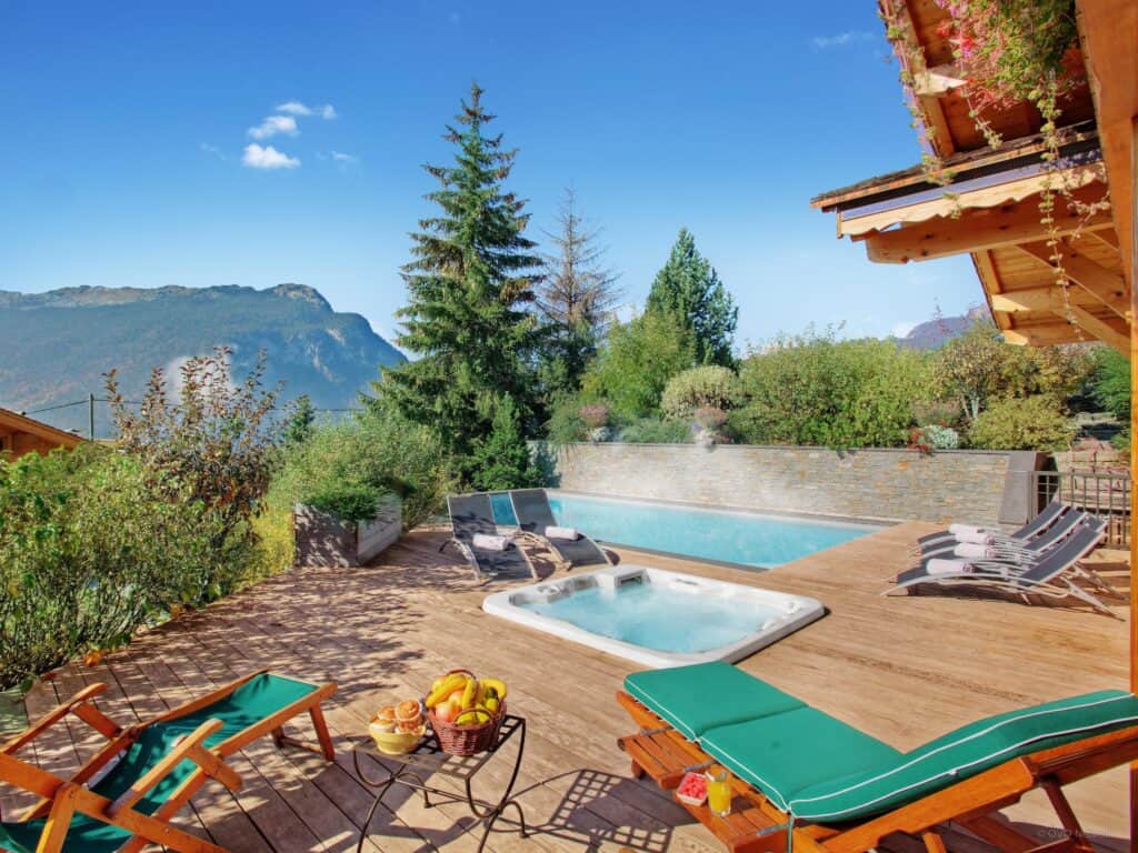 Terrasse d'été d'un chalet avec chaises longues, piscine et jacuzzi.