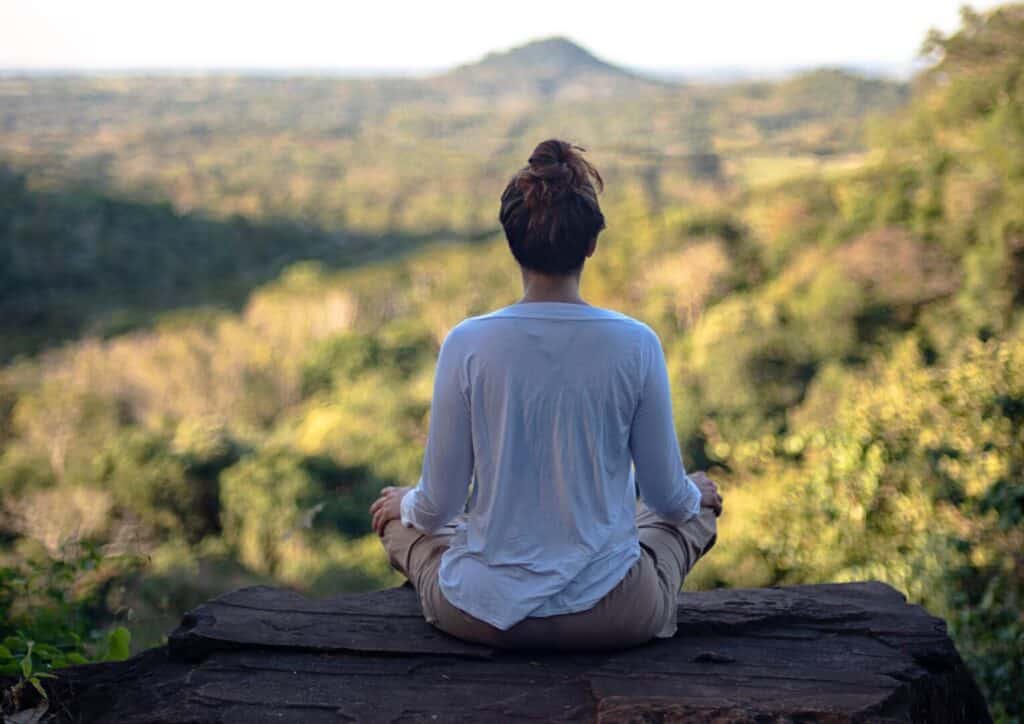 A woman enjoys a yoga session as she sits on a log contemplating the mountains in autumn