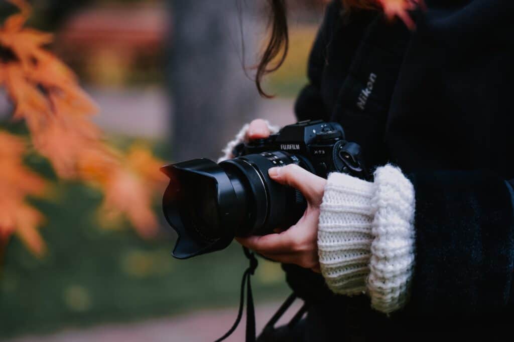 A woman holding a camera in front of some autumn leaves