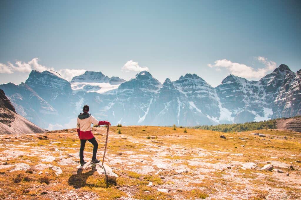 A walker stands on a rock, with his back to the camera, admiring the mountain view