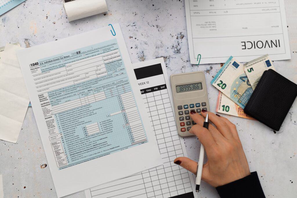 Une femme tapant à la calculatrice avec des factures et des billets sur une table. 