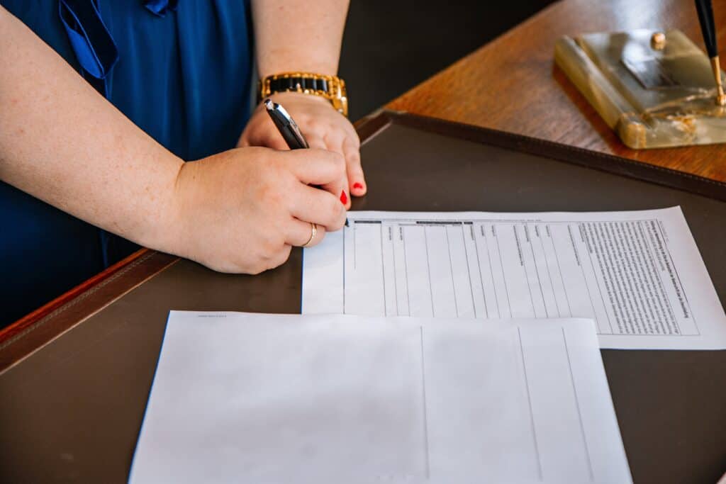 Une femme signant des documents sur un bureau en bois. 