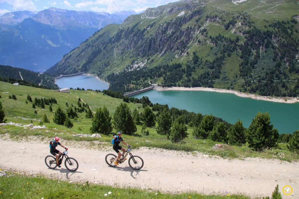 Deux cyclistes descendent un des sentiers de la Transmaurienne Vanoise, avec une rivière en arrière-plan.