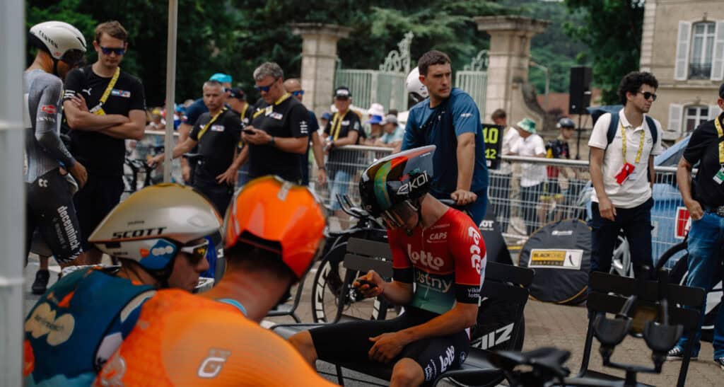 A Tour de France cyclist team around a bench in a town.